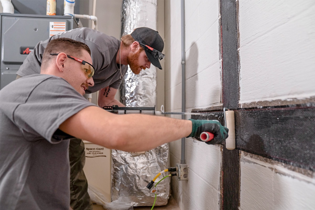 Foundation team applying epoxy on carbon fiber straps in a basement