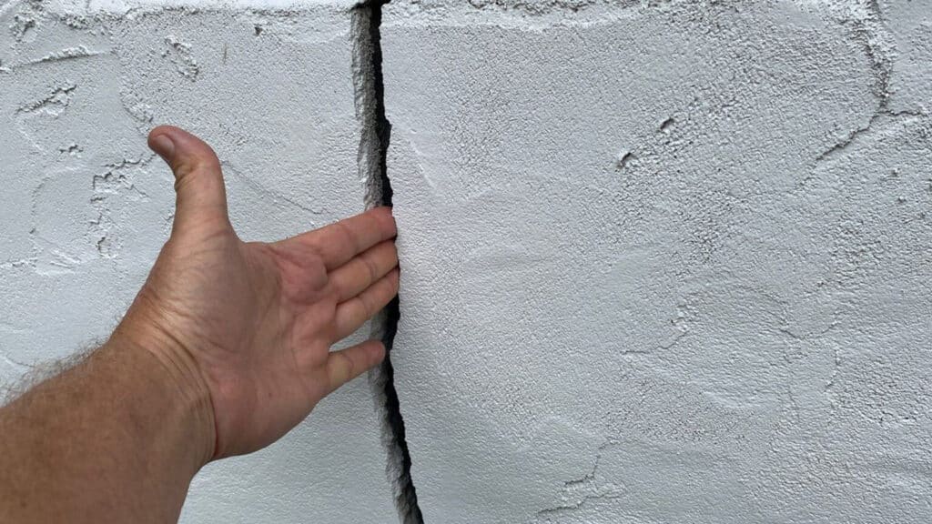 A man's hand fitting inside a foundation wall crack of a home