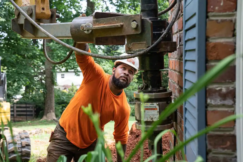 A foundation repair specialist installing a helical pier on a home