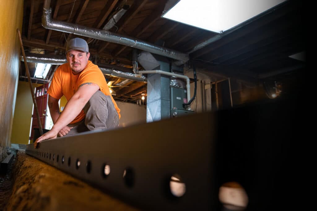 Man installing basement waterproofing channels in a home