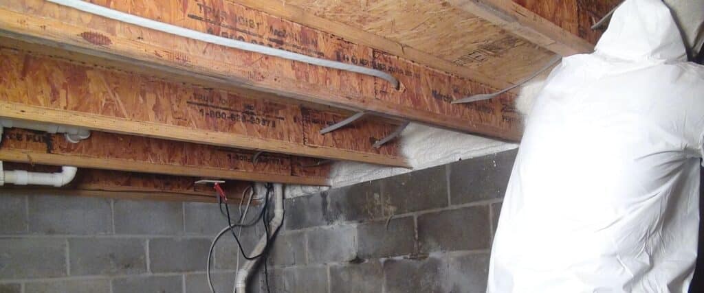 Person spraying foam insulation in a crawl space