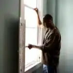 A man dealing with a stuck or jamming window in his home