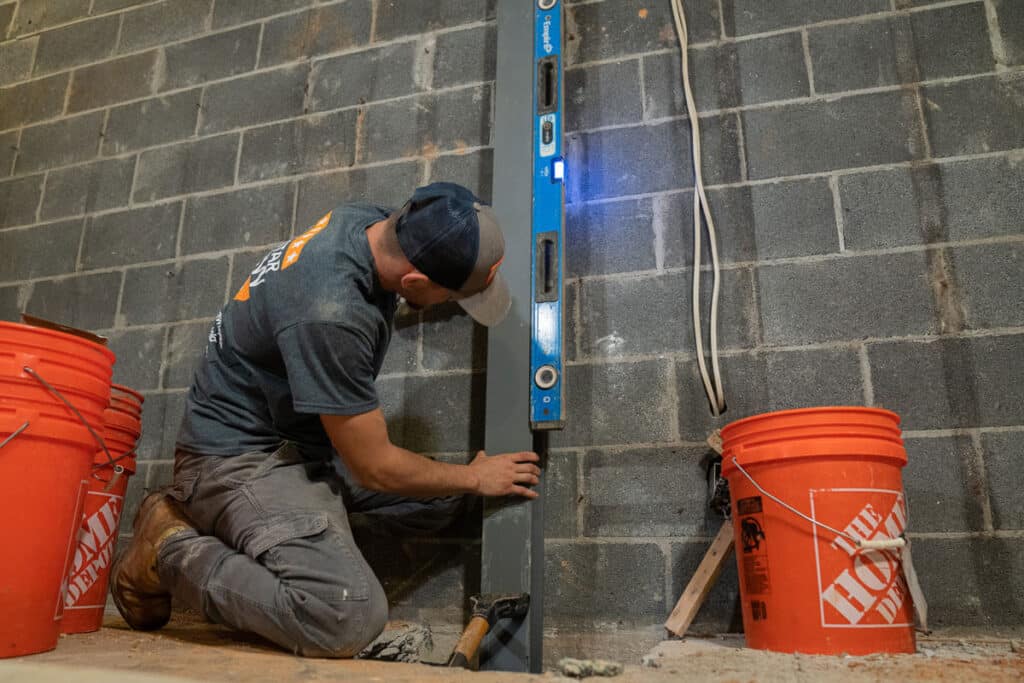Man measuring steel I-Beams for a basement wall reinforcement to prevent further bowing